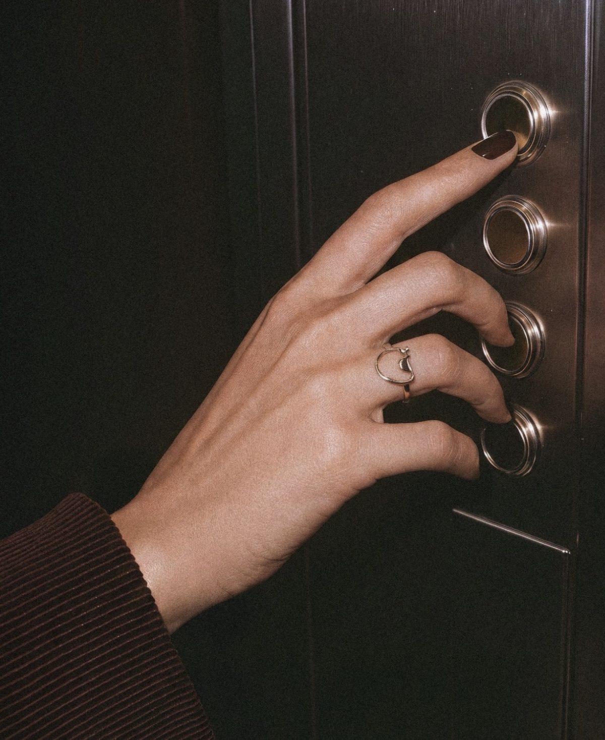 A hand wearing a gold ring, pressing an elevator button